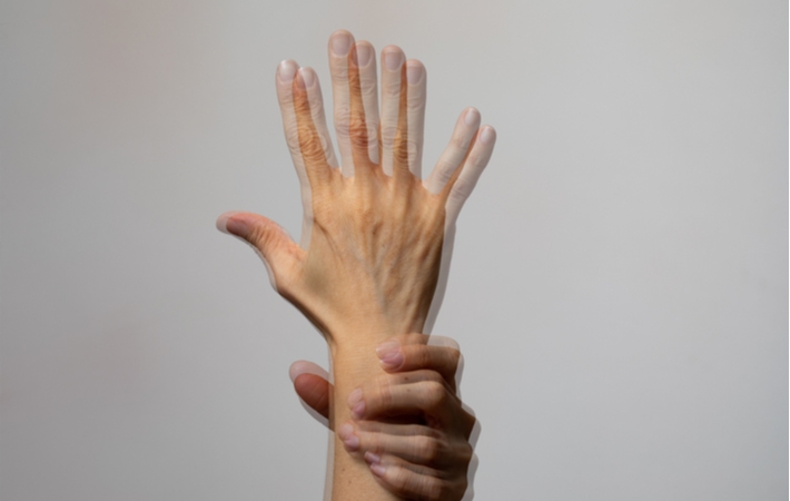 A close-up of what someone with double vision may see when looking at a hand raised straight up in the air, distorted and blurry