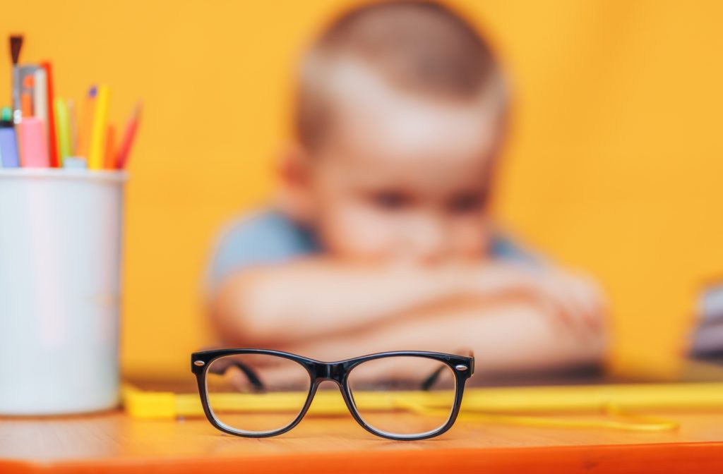 A young boy sitting in front of a pair of glasses on a table