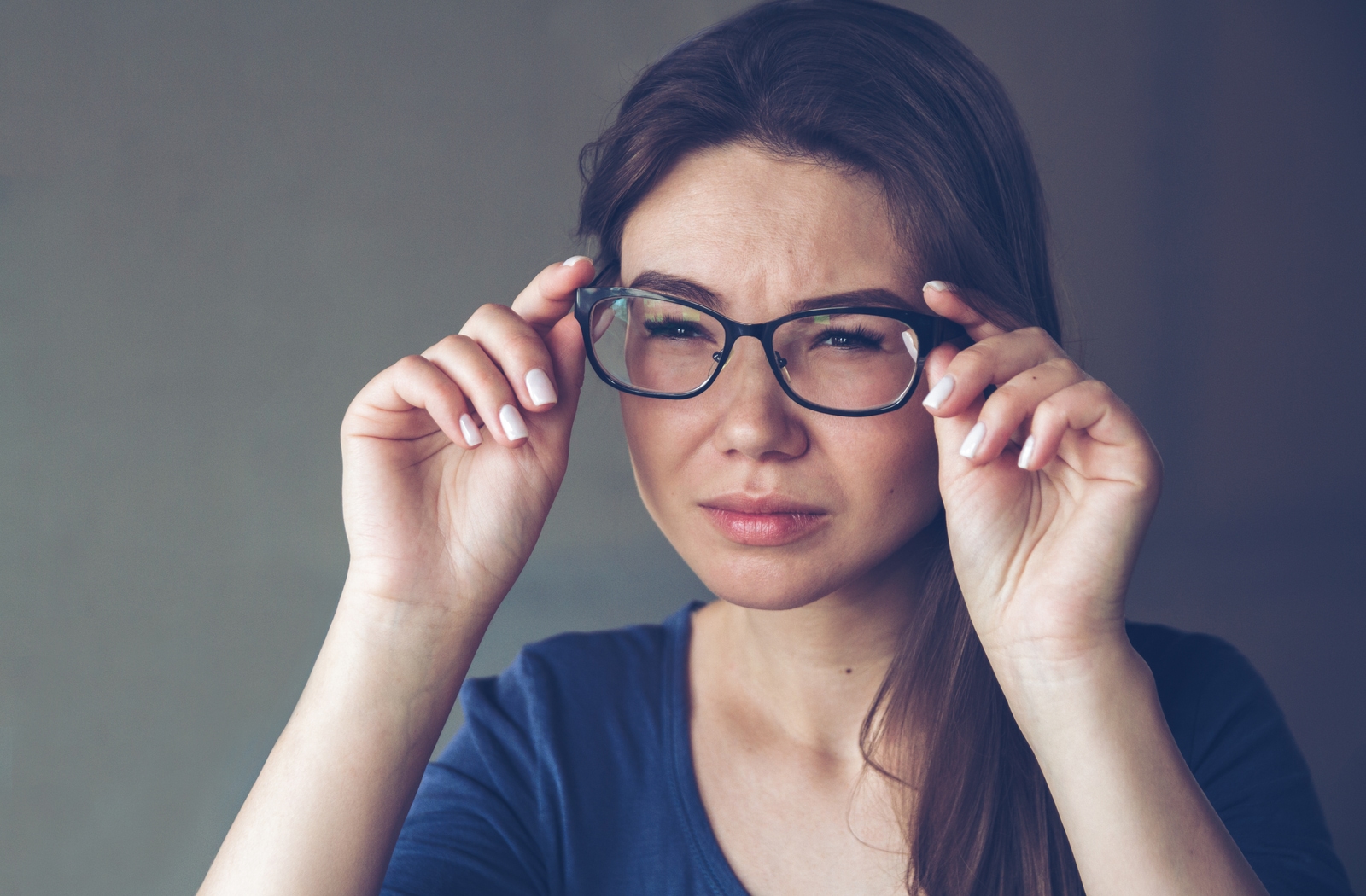 A woman with astigmatism squinting and holding onto her glasses