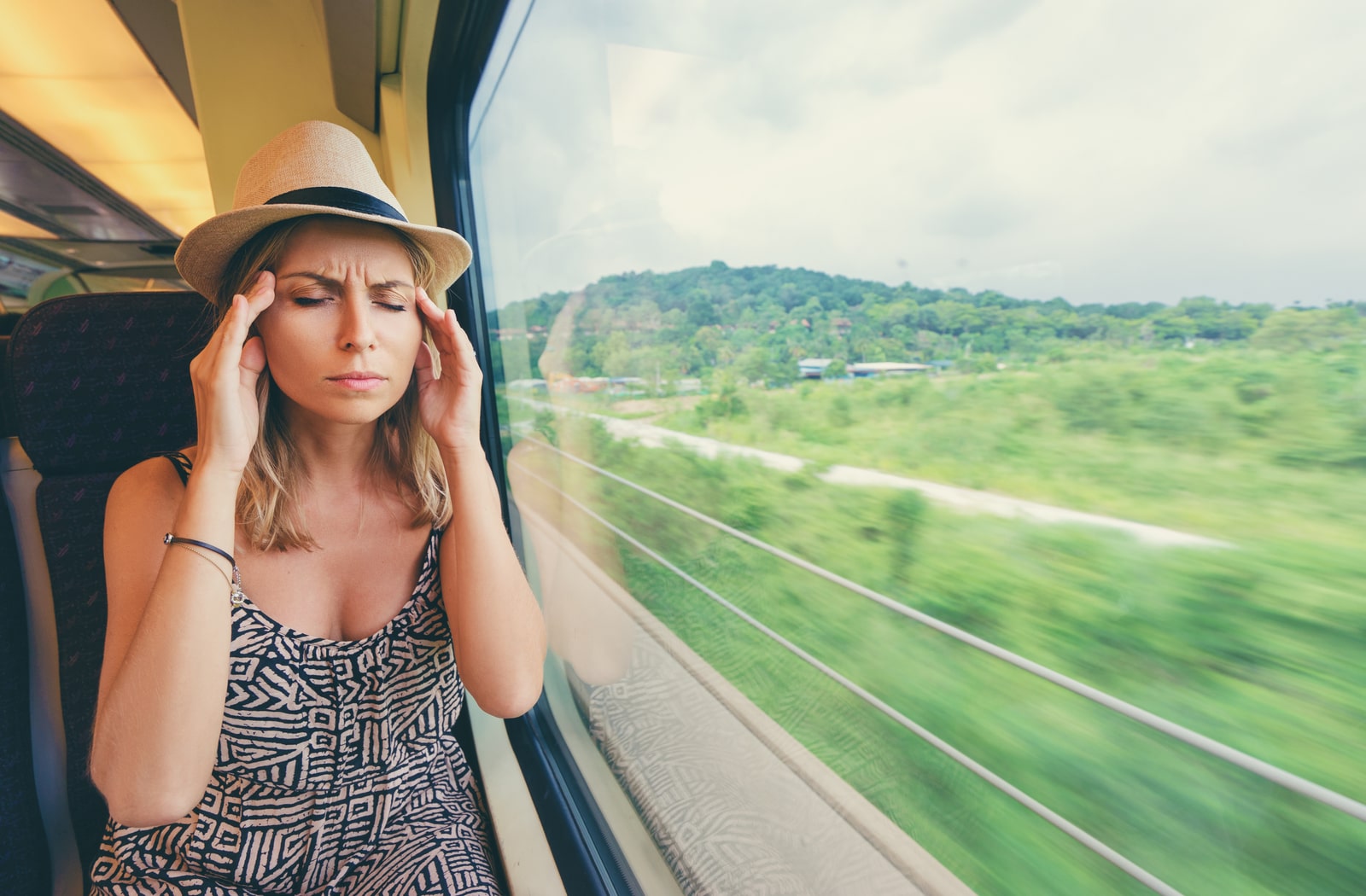 A woman riding the train with her hands on her temples, suffering from motion sickness